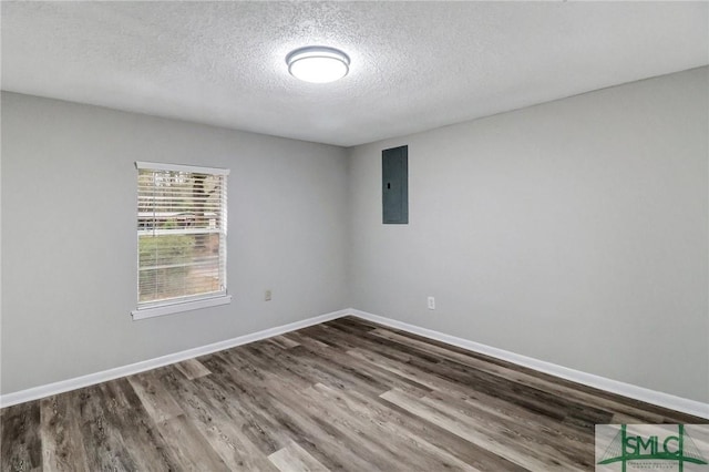 empty room with a textured ceiling, wood finished floors, electric panel, and baseboards