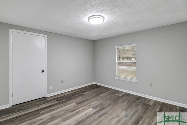 empty room featuring a textured ceiling, baseboards, and wood finished floors