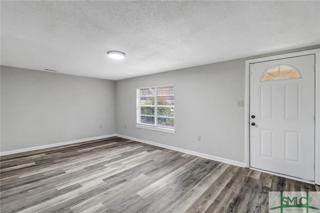 foyer entrance with a textured ceiling, wood finished floors, and baseboards