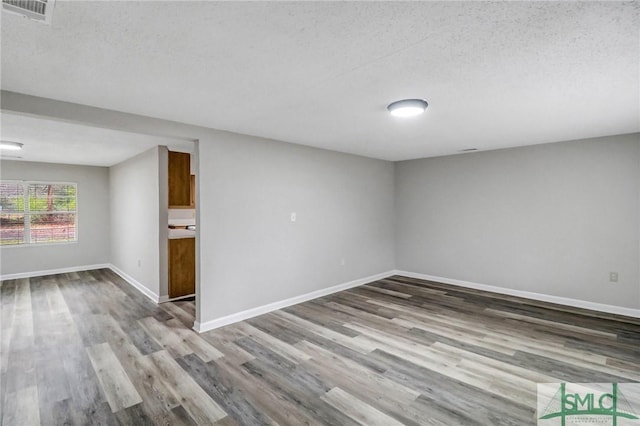 empty room featuring baseboards, a textured ceiling, visible vents, and wood finished floors