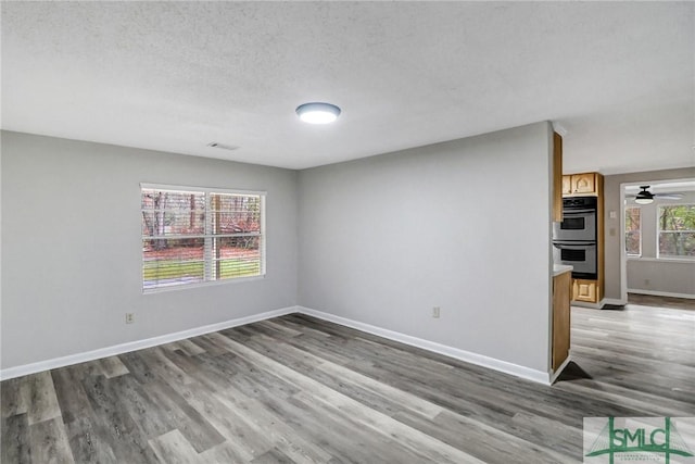 unfurnished room featuring a ceiling fan, light wood-style flooring, baseboards, and a textured ceiling