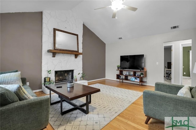 living area featuring a fireplace, lofted ceiling, visible vents, ceiling fan, and wood finished floors