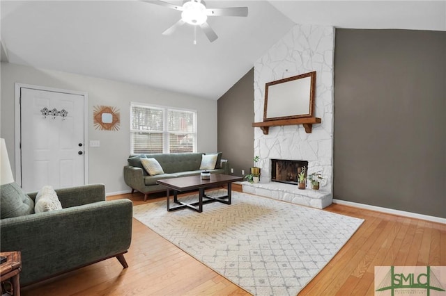 living room with baseboards, ceiling fan, wood finished floors, a fireplace, and high vaulted ceiling