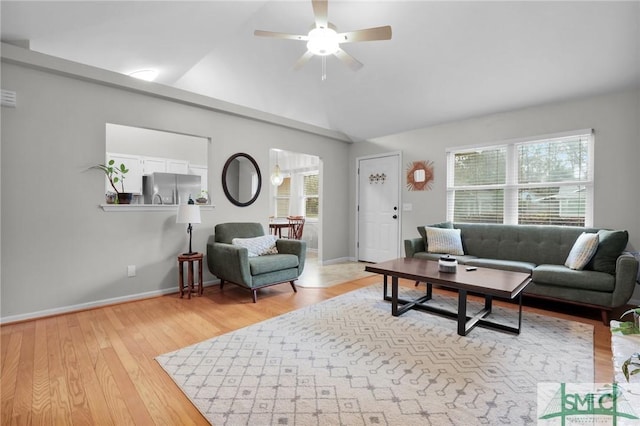 living room with a ceiling fan, lofted ceiling, baseboards, and light wood finished floors