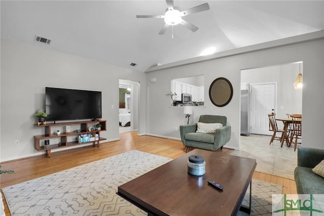 living room featuring lofted ceiling, light wood finished floors, visible vents, and a ceiling fan