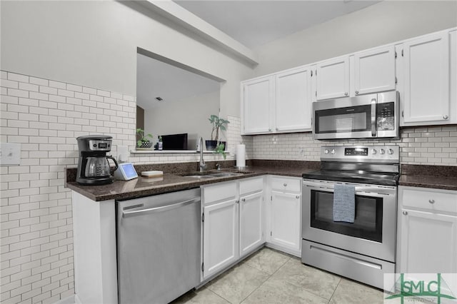 kitchen with light tile patterned floors, stainless steel appliances, white cabinets, a sink, and dark stone countertops