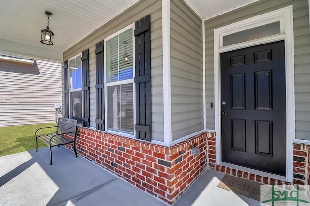 doorway to property featuring a porch and brick siding