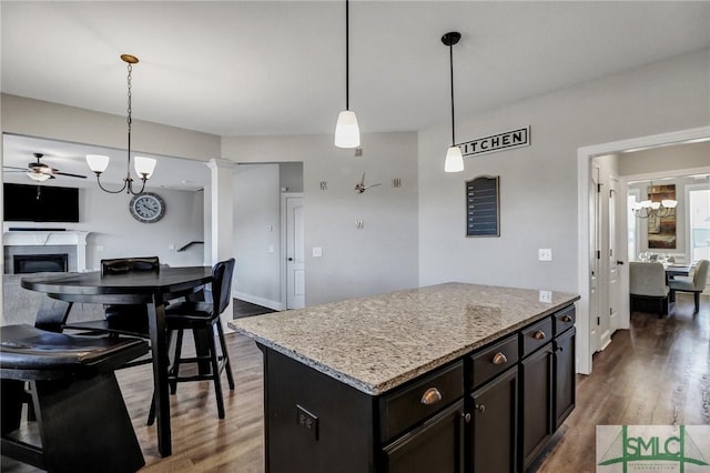 kitchen featuring a kitchen island, wood finished floors, a glass covered fireplace, decorative light fixtures, and ornate columns