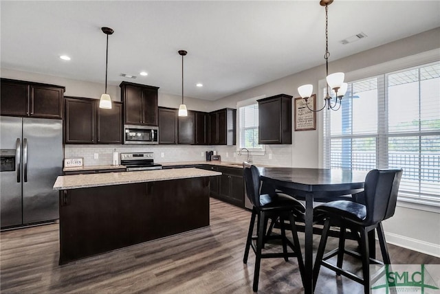 kitchen with tasteful backsplash, appliances with stainless steel finishes, a sink, dark brown cabinetry, and a kitchen island