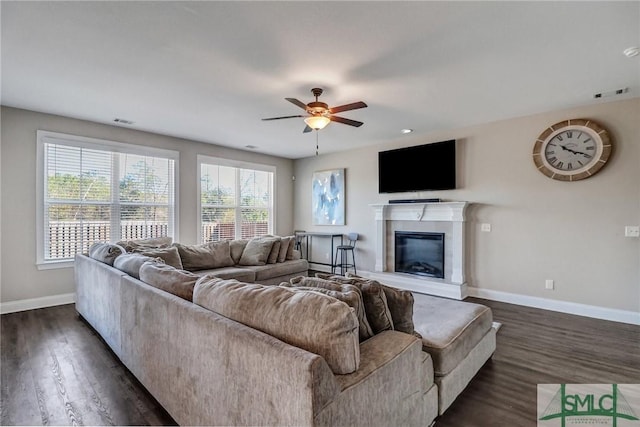 living area featuring dark wood finished floors, visible vents, a ceiling fan, a glass covered fireplace, and baseboards