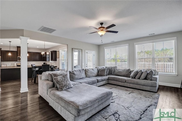 living area featuring dark wood-style flooring, visible vents, decorative columns, and baseboards