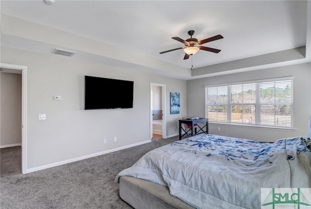 carpeted bedroom featuring baseboards, visible vents, ensuite bath, ceiling fan, and a tray ceiling