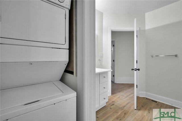 clothes washing area with stacked washer / dryer, light wood-type flooring, visible vents, and baseboards