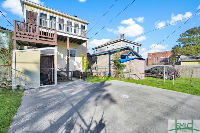 back of property featuring a balcony, fence, and a yard