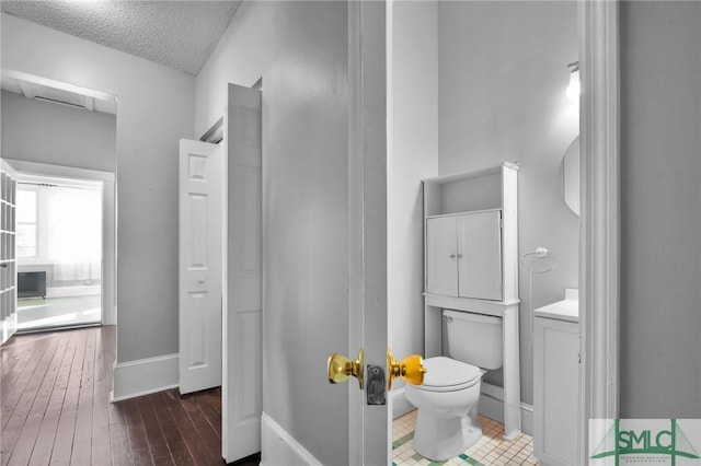 bathroom with baseboards, hardwood / wood-style floors, toilet, and a textured ceiling