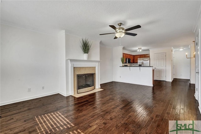 unfurnished living room featuring dark wood-style flooring, a ceiling fan, baseboards, ornamental molding, and a tiled fireplace