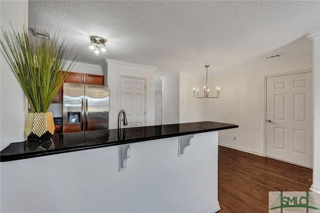 kitchen with stainless steel fridge with ice dispenser, dark countertops, dark wood-style floors, a kitchen breakfast bar, and a peninsula