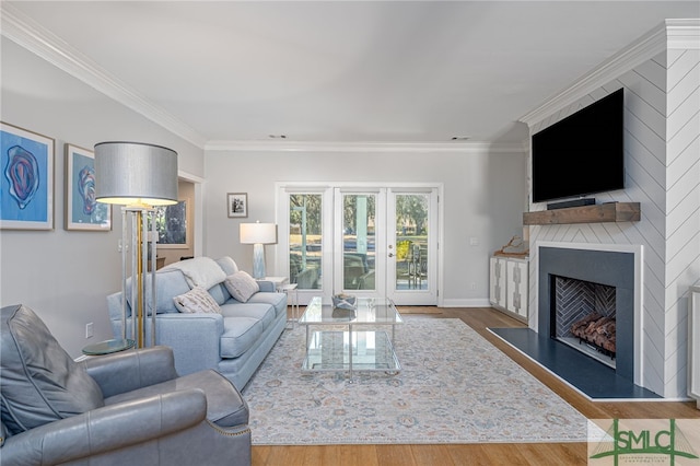 living area featuring baseboards, wood finished floors, a large fireplace, and ornamental molding