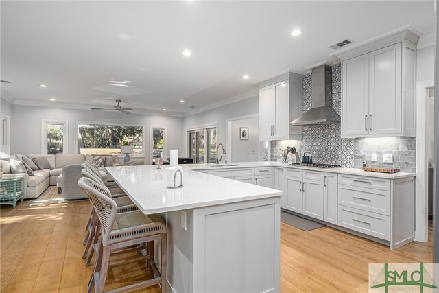 kitchen featuring wall chimney range hood, a breakfast bar area, a sink, visible vents, and light wood-style floors