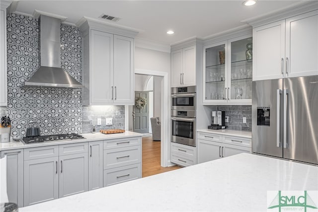 kitchen with stainless steel appliances, wall chimney range hood, ornamental molding, backsplash, and visible vents