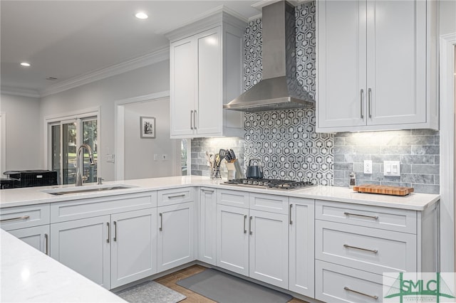 kitchen featuring stainless steel gas stovetop, decorative backsplash, ornamental molding, a sink, and wall chimney exhaust hood