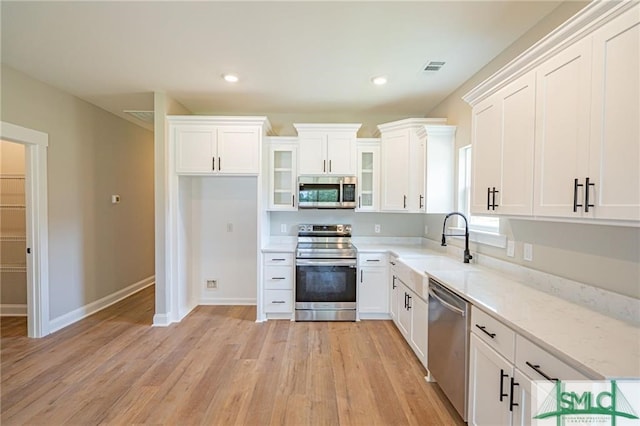 kitchen with stainless steel appliances, glass insert cabinets, white cabinets, a sink, and light wood-type flooring