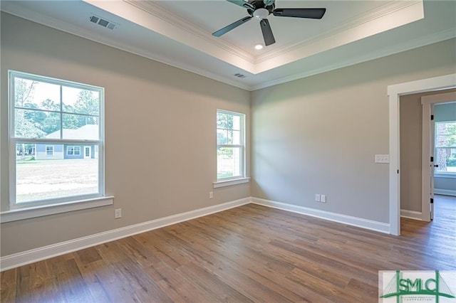 empty room with a raised ceiling, visible vents, plenty of natural light, and wood finished floors