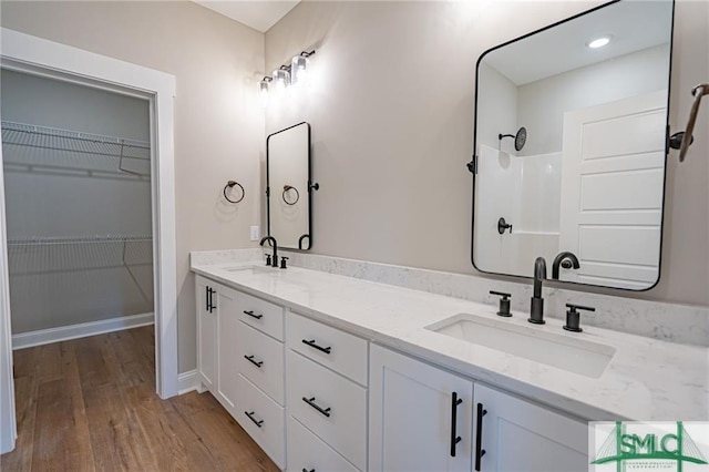 full bath with double vanity, wood finished floors, a sink, and a walk in closet