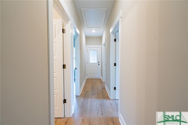 hallway featuring attic access, baseboards, and light wood finished floors