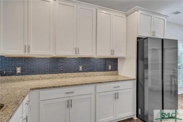 kitchen featuring light stone counters, decorative backsplash, white cabinetry, and freestanding refrigerator