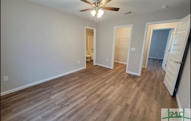 unfurnished bedroom featuring wood finished floors, visible vents, baseboards, a spacious closet, and a closet