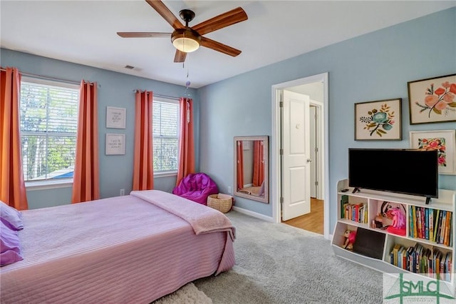 carpeted bedroom with baseboards, multiple windows, visible vents, and a ceiling fan