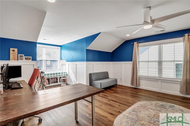 home office with ceiling fan, a wainscoted wall, wood finished floors, visible vents, and vaulted ceiling