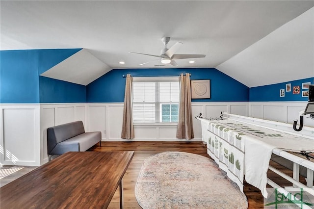 bedroom with a ceiling fan, a wainscoted wall, vaulted ceiling, and wood finished floors