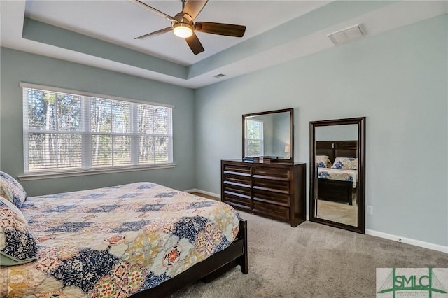 carpeted bedroom featuring a raised ceiling, visible vents, and baseboards