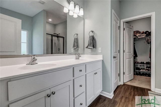 bathroom featuring double vanity, a stall shower, visible vents, wood finished floors, and a sink