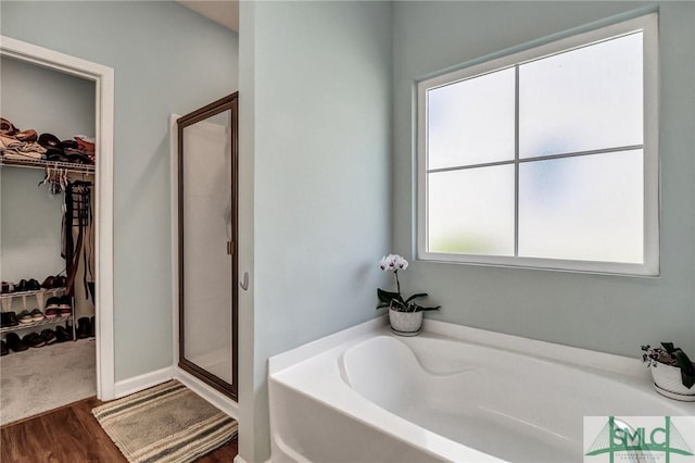 bathroom featuring a shower stall, a spacious closet, a bath, and wood finished floors