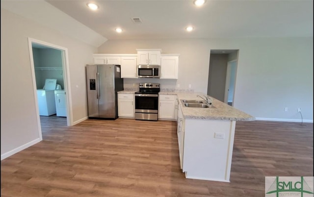 kitchen featuring washing machine and dryer, a peninsula, a sink, white cabinets, and appliances with stainless steel finishes