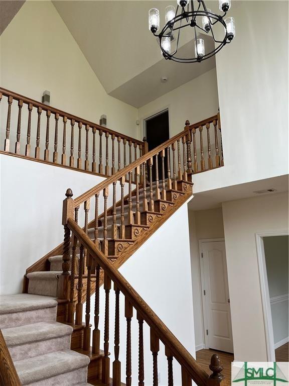 staircase with visible vents, high vaulted ceiling, and a notable chandelier