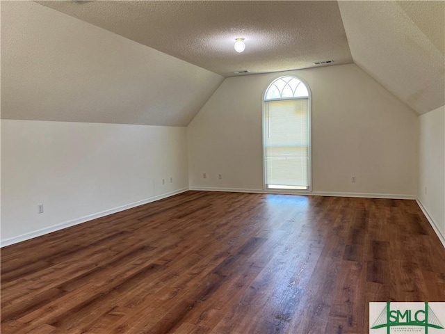 additional living space featuring a textured ceiling, lofted ceiling, dark wood-style flooring, visible vents, and baseboards