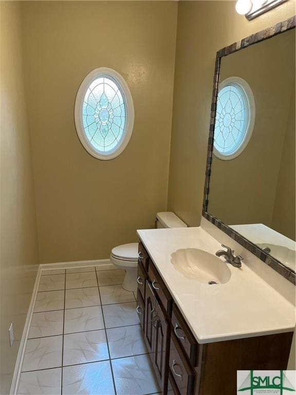 half bathroom with toilet, marble finish floor, baseboards, and vanity