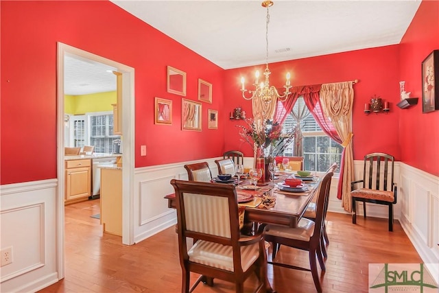 dining area featuring light wood-style flooring, a chandelier, a wainscoted wall, and visible vents