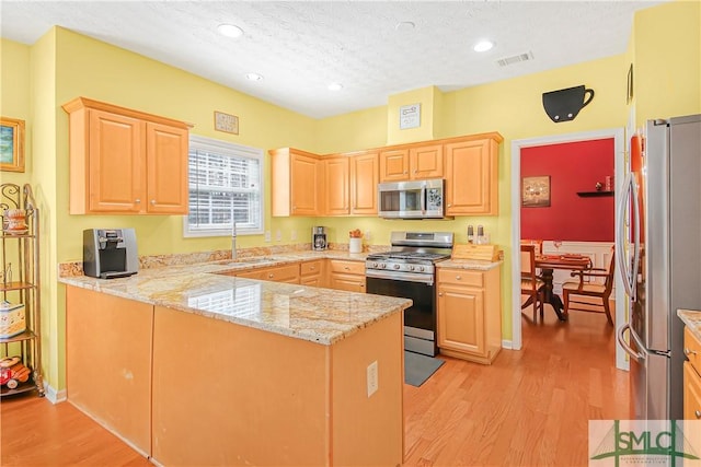 kitchen featuring visible vents, a peninsula, stainless steel appliances, light brown cabinetry, and a sink