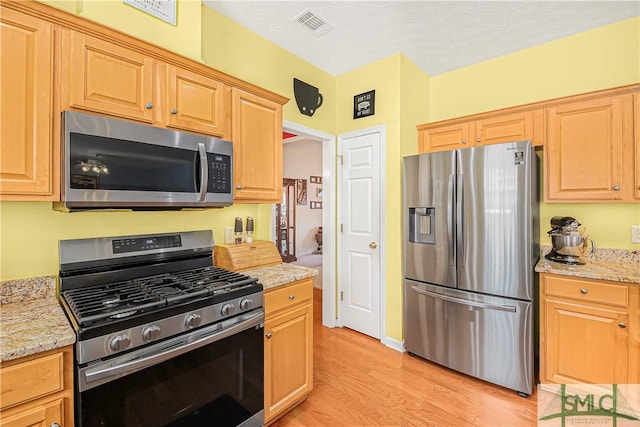 kitchen with light wood finished floors, visible vents, appliances with stainless steel finishes, light stone countertops, and a textured ceiling