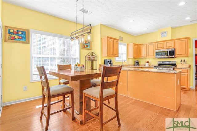 kitchen featuring stainless steel microwave, visible vents, light wood-style flooring, light brown cabinets, and range