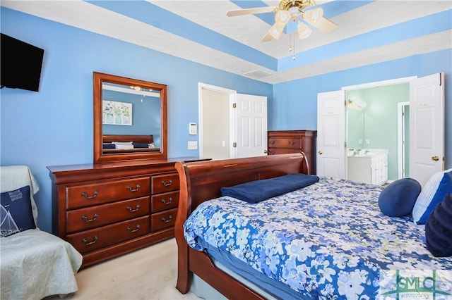 bedroom featuring ceiling fan, light colored carpet, visible vents, a tray ceiling, and ensuite bath