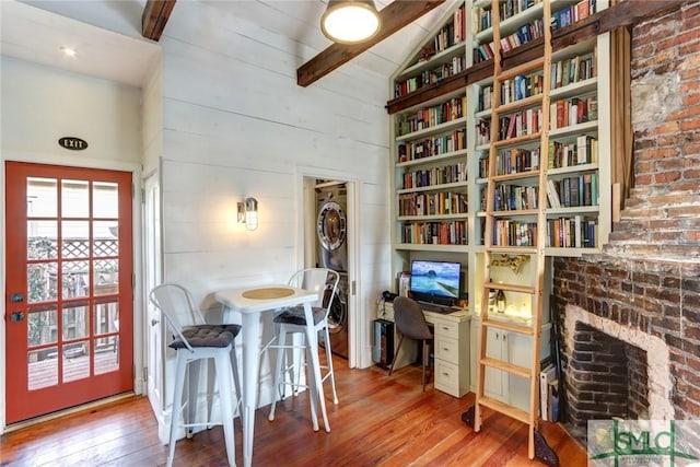 dining space with vaulted ceiling with beams, wood-type flooring, and a brick fireplace