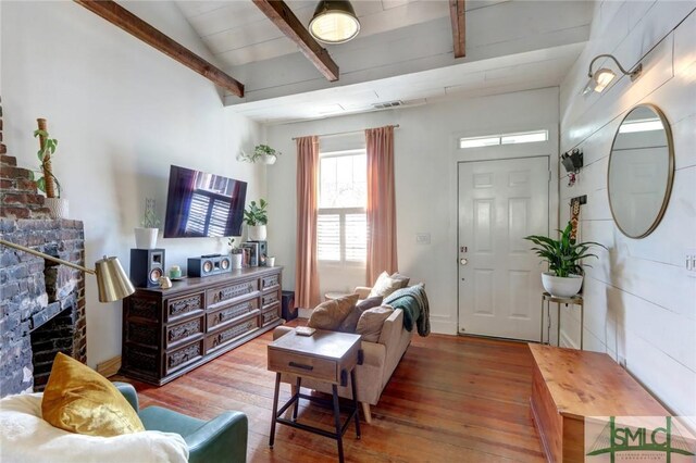 living room featuring beam ceiling, visible vents, a fireplace, and wood-type flooring