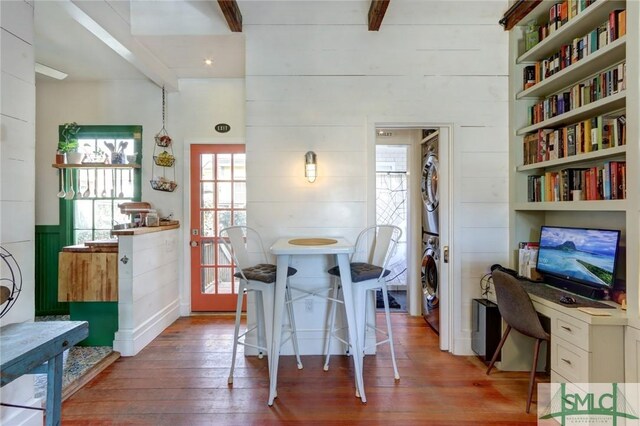 dining room with stacked washer / dryer, built in study area, wood walls, beamed ceiling, and hardwood / wood-style floors