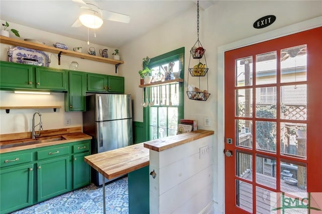 kitchen featuring a sink, wood counters, freestanding refrigerator, open shelves, and green cabinetry